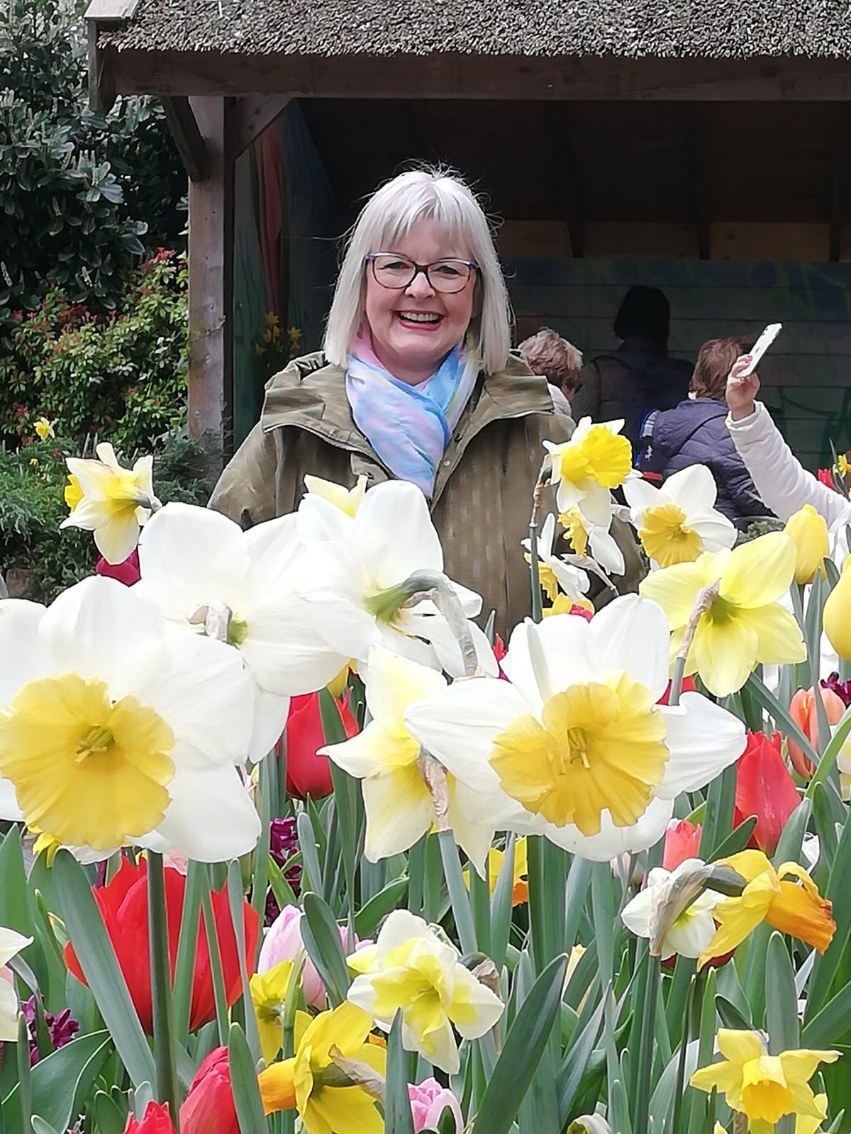 Frau Sbosny, unsere 1. Vorsitzende, steht vor einem Meer aus gelb-weißen Osterglocken und roten Tulpen.