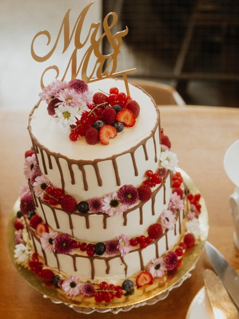 Die 3-stöckige Hochzeitstorte war mit heller Sahnecreme eingedeckt und auf allen 3 Stufen mit roten Beerenfrüchten und kleinen Blumen umkränzt.