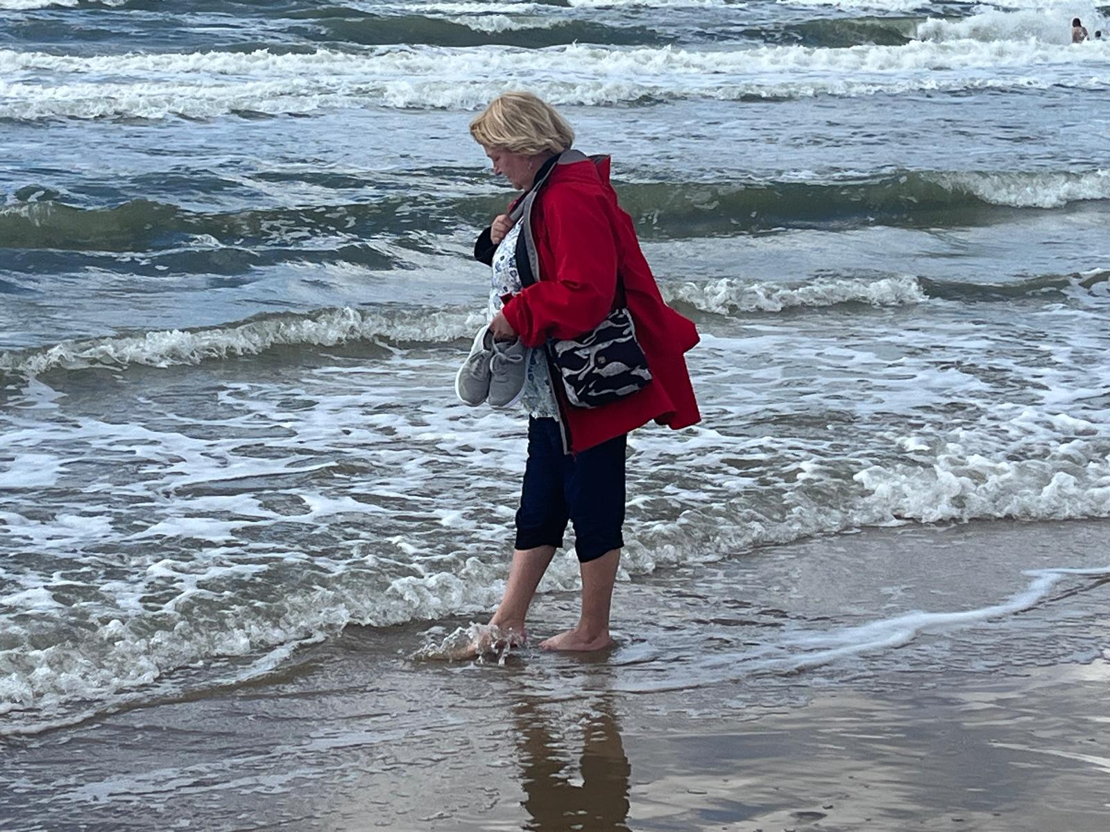 Barfuß durch die Wellen - eine Seniorin zog Schuhe und Strümpfe aus und ging mit den bloßen Füßen durchs Wasser.