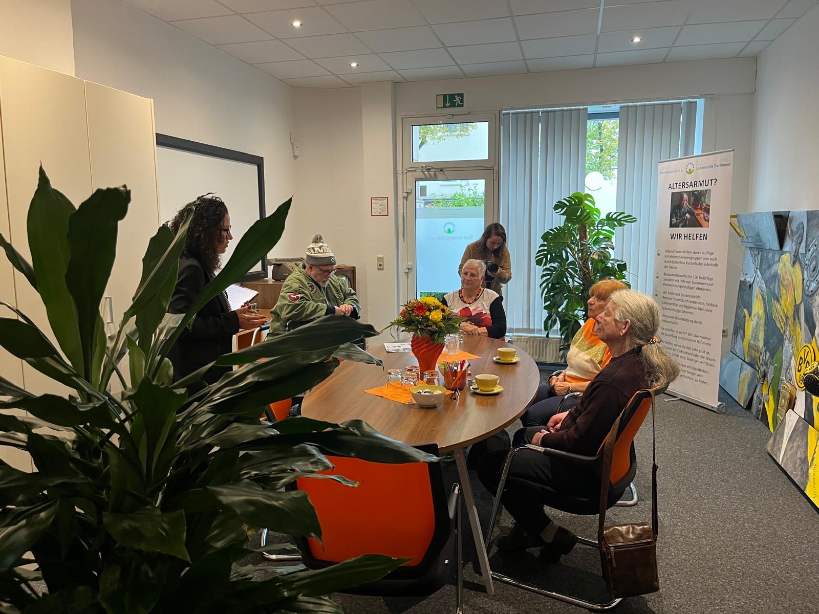 Altersarmut? Wir helfen! - steht auf dem Plakat rechts. Das Kamerateam spricht drei Senioren.