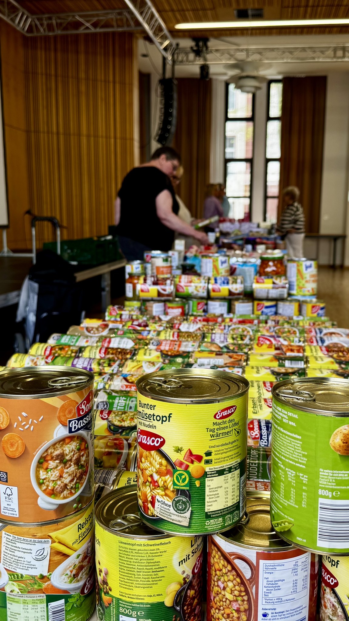 findet grundsätzlich im Gemeindehaus Dortmund-Hörde statt. Im Vordergrund auf der Seniorentafel befinden sich Konservendosen mit verschiedenen Fertiggerichten.