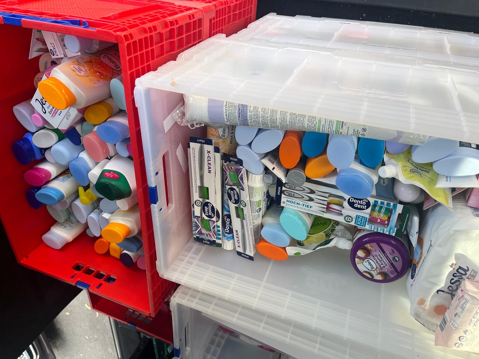 2 Kisten - eine rote und eine weiße - mit Hygieneartikeln wie Badezusatz, Duschgel, Haarshampoo, Zahnpasta und Zahnbürsten.