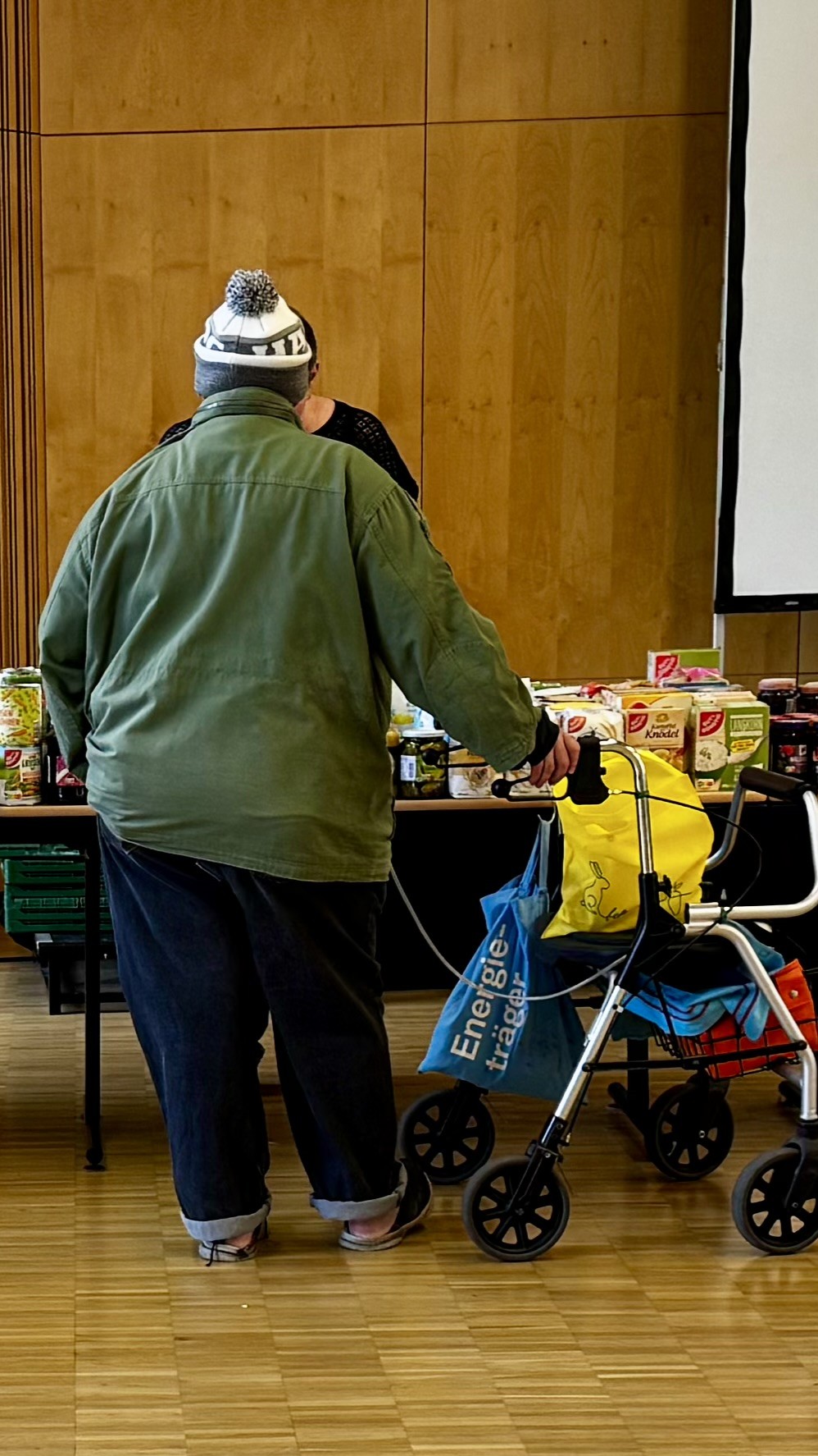 im Gemeindehaus steht eine Besucherin vor haltbaren Lebensmitteln wie z.B. Kartoffel-Knödel, Reis und Weizenmehl.