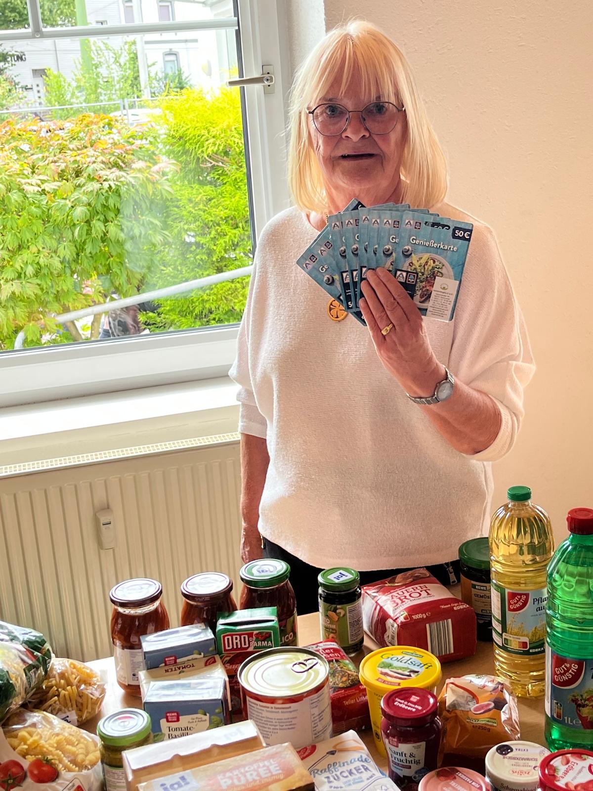 Eine Seniorin bei der Seniorentafel in Körne hält 10 Lebensmittel-Gutscheine von ALDI in der Hand.