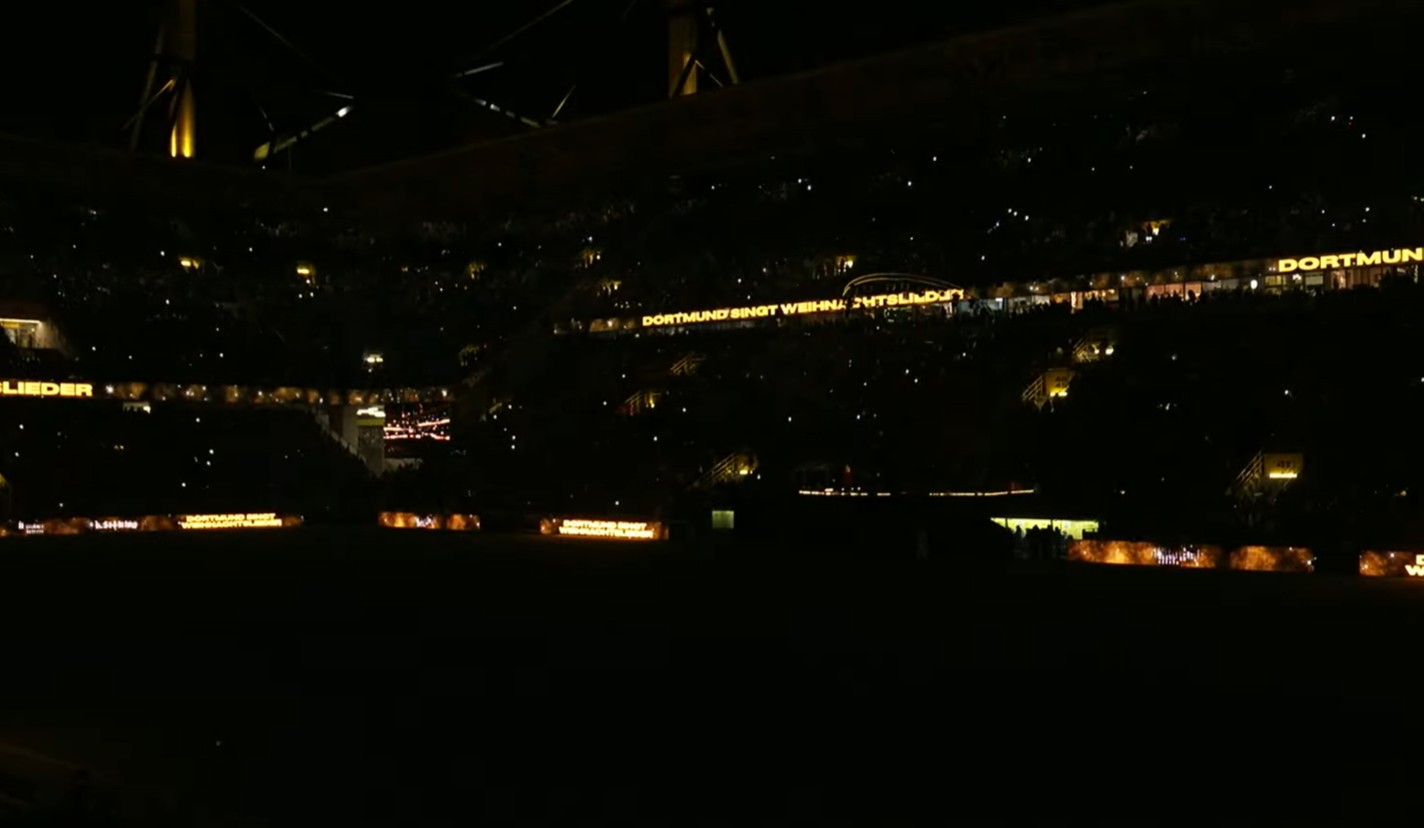 Im hellerleuchteten Stadion steht rundherum in großen leuchtend gelben Leucht-Buchstaben: DORTMUND SINGT WEIHNACHTSLIEDER