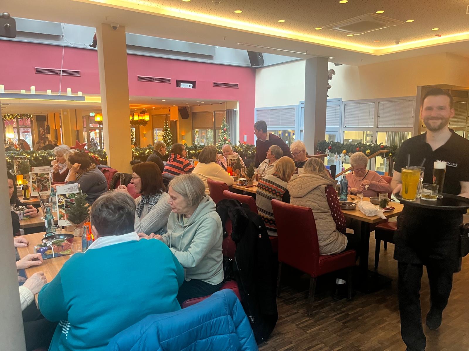 Getränke werden serviert - Ein Kellner bringt ein Tablett mit je einem Glas Bier, Wasser und Apfelschorle herein.