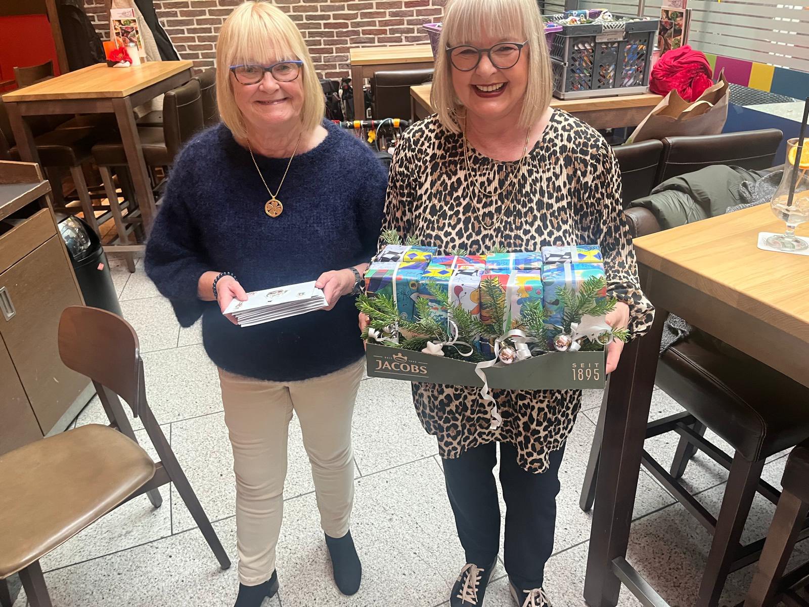 Frau Sbosny, die Erste Vorsitzende des Seniorenglück e.V., (rechts) und eine andere ehrenamtliche Mitarbeiterin (links) halten kleine Geschenke und Briefumschläge mit Lebensmittelgutscheinen bereit.
