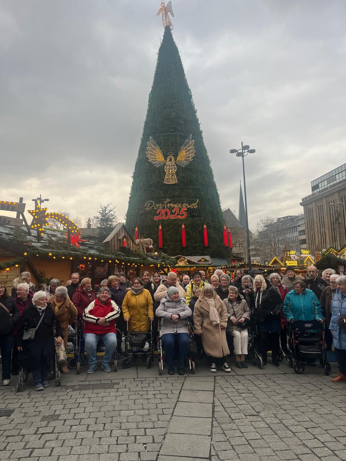 Gruppenfoto aller beteiligten Seniorinnen und Senioren vor dem riesigen Weihnachtsbaum auf dem Dortmunder Weihnachtsmarkt 2025