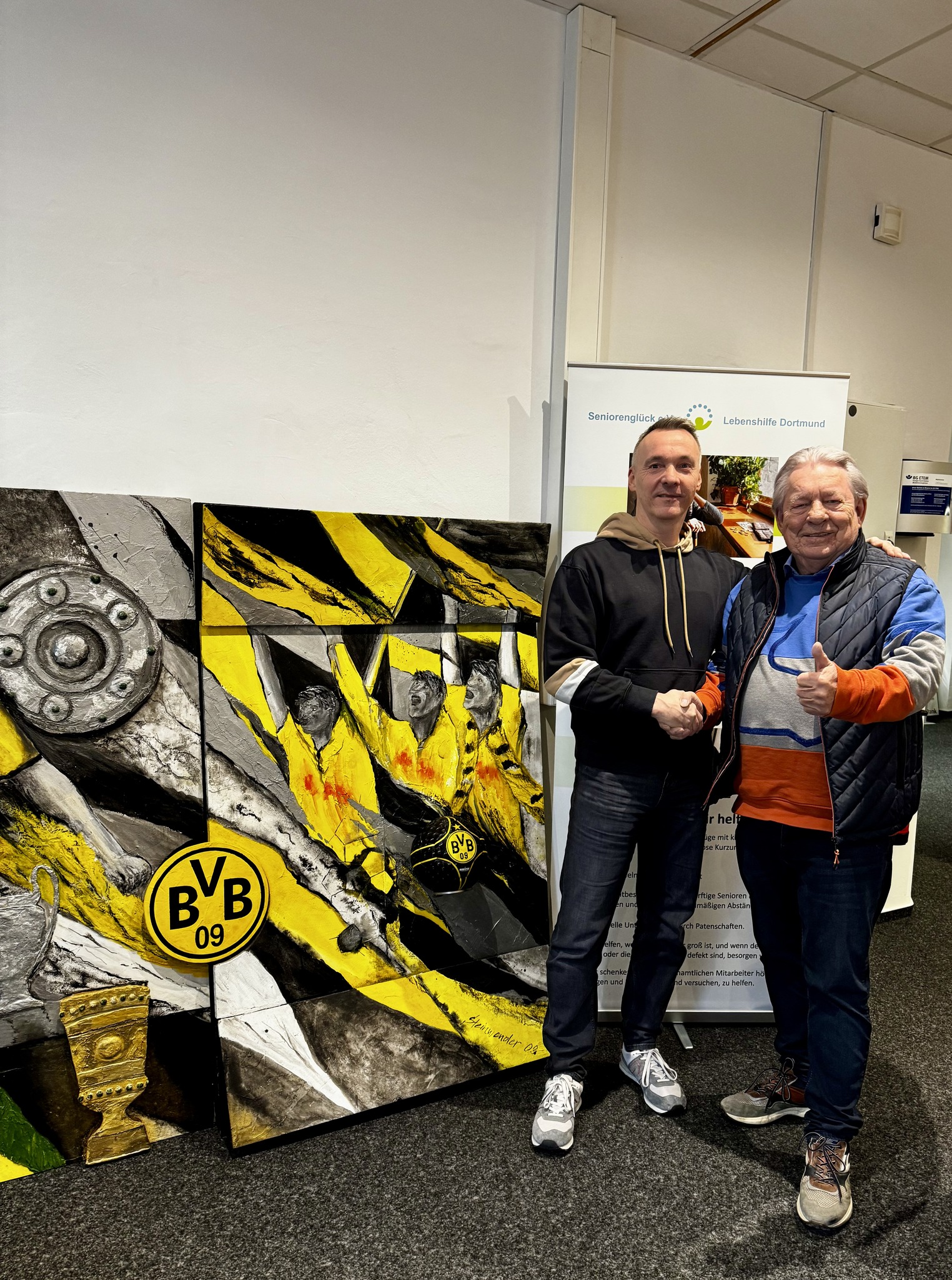 Dirk Eckardt, Vorstand der Stiftung Lebenskraft, (links) und Hans Schwarz vom Seniorenglück e.V. (rechts) neben dem BVB-Wandbild