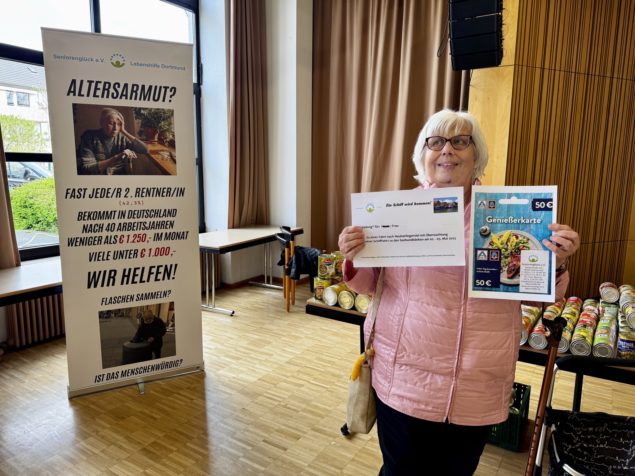 Eine Seniorin hält mit dankbarem Blick die Einladung zum Ausflug nach Neuharlingersiel und einen Lebensmittel-Gutschein von ALDI in den Händen.