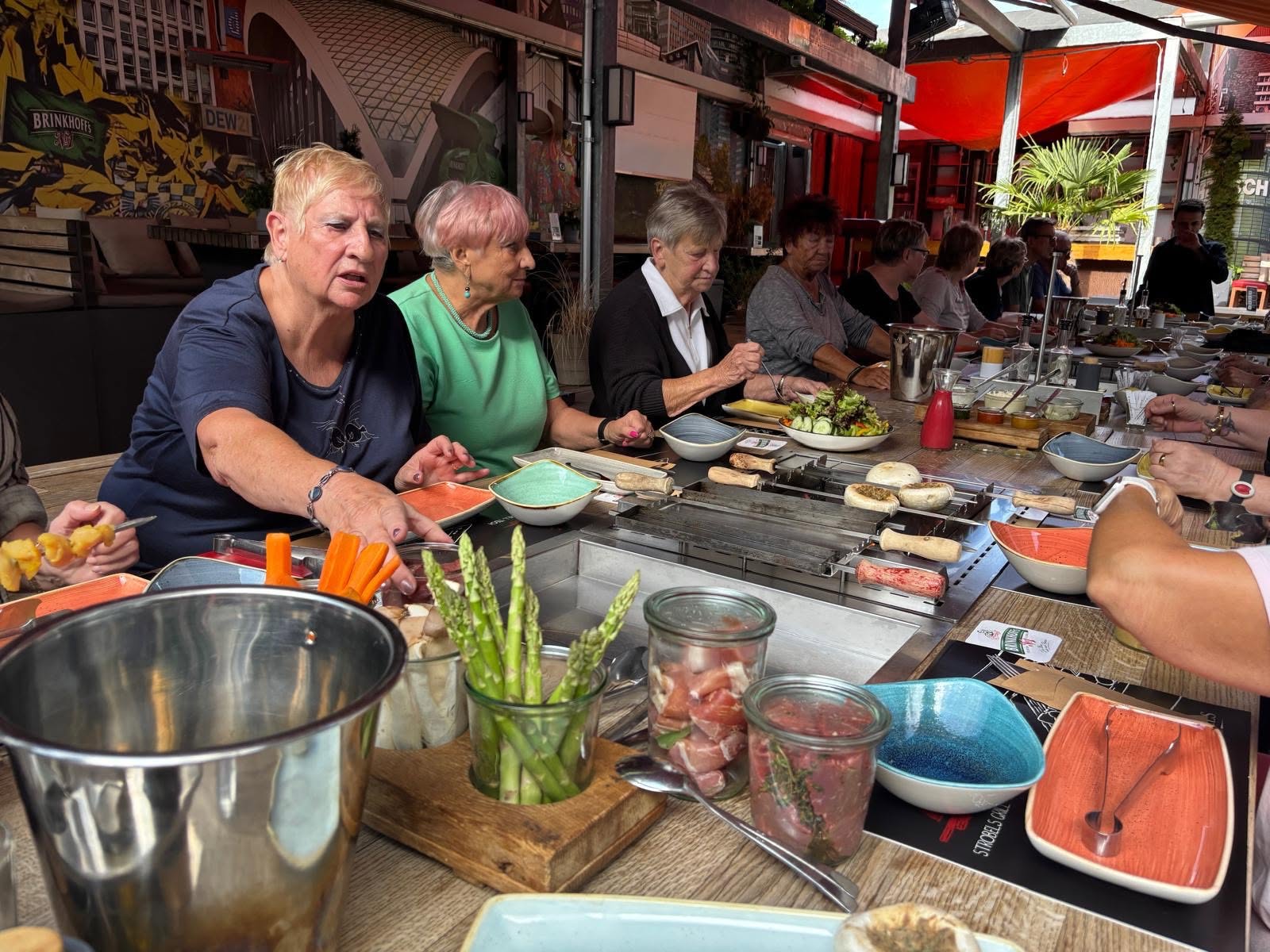 Die Gäste legen das Fleisch auf den Grill, im Vordergrund weißer und grüner Spargel sowie Möhren-Sticks.