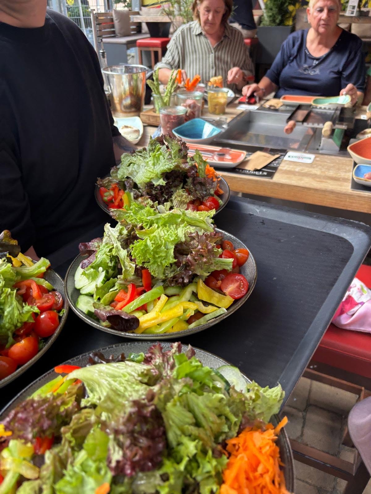 Der Kellner serviert bunte Salat-Teller - mit Frisée-Salat, geraspelten Möhren, Tomaten und bunten Paprika-Streifen.